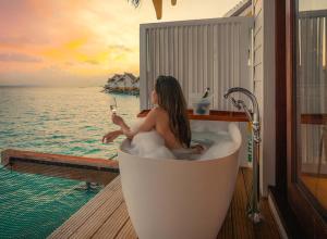 una mujer sentada en una bañera con una copa de vino en SAii Lagoon Maldives, Curio Collection By Hilton en South Male Atoll