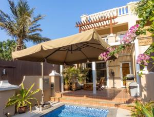 - un parasol au-dessus d'une piscine en face d'une maison dans l'établissement Dar 66 Plunge Pool Resort Townhouses, à Ras al Khaimah