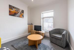 ein Wohnzimmer mit einem Stuhl, einem Tisch und einem TV in der Unterkunft Chesterfield Lodge - 2 Bedroom Apartment near Chesterfield Town Centre in Chesterfield