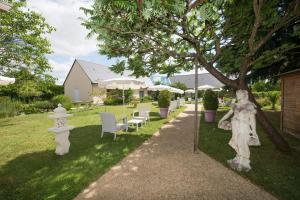 un jardín con estatuas blancas, mesas y sombrillas en Logis Auberge Bienvenue en Doué-la-Fontaine