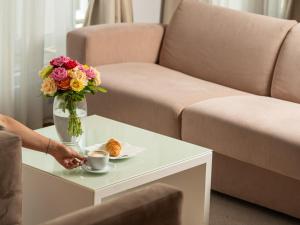 a person holding a cup of coffee and a vase of flowers on a table at Garni Hotel Centar in Novi Sad