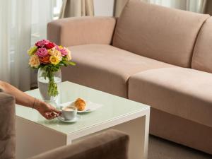 eine Person, die eine Tasse Kaffee und eine Vase Blumen auf dem Tisch hält in der Unterkunft Garni Hotel Centar in Novi Sad