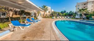 a swimming pool with blue lounge chairs next to a building at Modern Pool View Studio Apartment in Caesar Resort & SPA, Long Beach in Saint Yeorgios