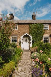 uma casa de tijolos com uma porta branca e algumas flores em Swallow Cottage, Bakewell em Bakewell