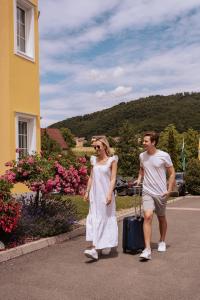 a man and a woman walking down a road with a suitcase at Schlössl Hotel Kindl in Bad Gleichenberg