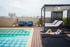 een vrouw op een bed naast een zwembad bij THEA Serviced Apartment by TH District, SHA Extra Plus in Bangkok