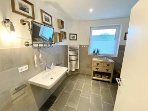 uma casa de banho com um lavatório e uma televisão na parede em Sandpiper em Gelting