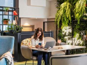 a woman sitting at a table with a laptop at Novotel Rennes Alma in Rennes