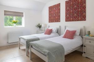 two beds in a white room with red pillows at Farmyard Cottage in Malmesbury