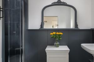 a bathroom with a mirror and a vase of yellow flowers at Little Calf Cottage in Malmesbury