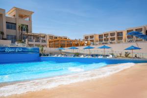 a swimming pool next to a beach with blue umbrellas at Cleopatra Luxury Resort Sharm - Adults Only 16 years plus in Sharm El Sheikh