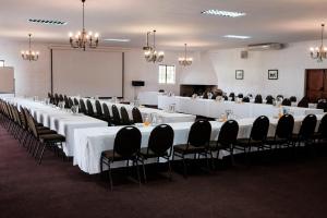 Houw Hoek Hotel في بوتريفيير: قاعة اجتماعات مع طاولات بيضاء وكراسي سوداء
