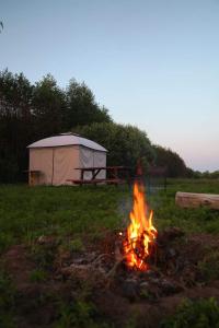 a camp fire in a field with a tent at Krastmslas in Smaltāni