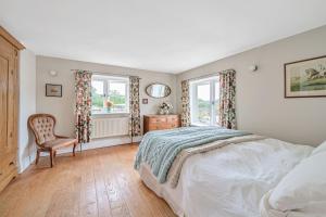 a bedroom with a bed and a chair and windows at Beech Cottage in Honiton