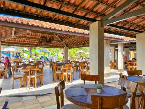 un restaurante con mesas y sillas de madera y gente de fondo en Jangadeiro Praia Hotel Resort - Pé na Areia, en Aquiraz