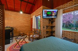 um quarto com uma cama e uma televisão numa parede de tijolos em Chalé Flores e Amores em Visconde de Mauá