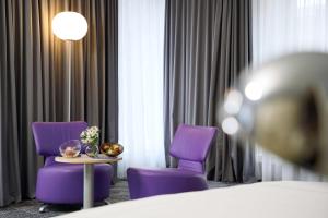 um quarto de hotel com cadeiras roxas, uma mesa e uma cama em Park Plaza Berlin em Berlim