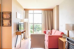 a hotel room with a pink couch and a window at Flat completo e charmoso Brasil 21 Suítes in Brasilia