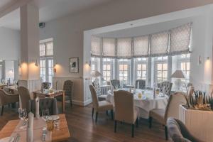 a dining room with tables and chairs and windows at Strandhotel Glücksburg in Glücksburg