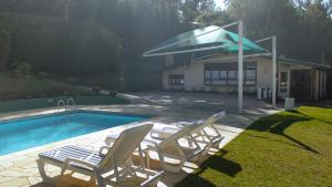 two lawn chairs and a pool with a umbrella at Casa com lareira e lazer, em Campos do Jordao SP in Campos do Jordão