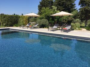 a swimming pool with two chairs and two umbrellas at Le Mas Terre Des Anges Gite in Sarrians