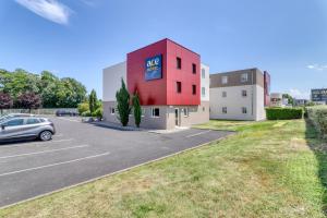 un edificio rosso con un'auto parcheggiata in un parcheggio di Ace Hôtel Clermont Ferrand La Pardieu a Clermont-Ferrand