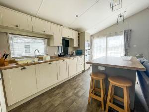 a kitchen with white cabinets and two bar stools at Beautiful Lodge With Decking At Breydon Water Park In Norfolk Ref 10022b in Belton
