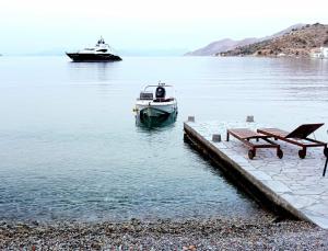 a boat in the water next to a table and a bench at Symi . VILLA CALME (Sur la Mer). in Symi