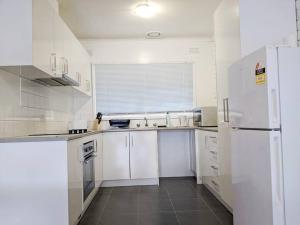 cocina con armarios blancos y nevera blanca en *Promo* 2-Bedroom Villa Next to Train Station!, en Melbourne