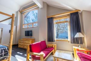 1 dormitorio con silla roja, 1 cama y ventanas en Brewster Mountain Lodge, en Banff