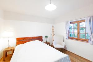 a white bedroom with a bed and a chair at Zimmer am Weinberg in Deutschlandsberg