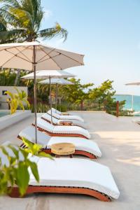 a row of white lounge chairs with an umbrella at Puerta del Cielo Hotel Origen in Bacalar