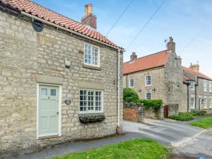 a stone cottage with a white door and a street at Maple Cottage in Slingsby