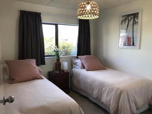2 łóżka w sypialni z oknem i żyrandolem w obiekcie Vicroad The Mount w mieście Mount Maunganui