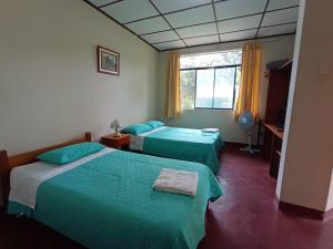 2 camas en una habitación con sábanas verdes y una ventana en BUNGALOWS EL RANCHO, en San Ramón