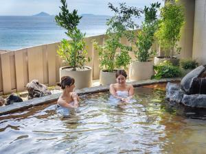 dos chicas en un jacuzzi con el océano en el fondo en Atagawa Ocean Resort, en Higashiizu