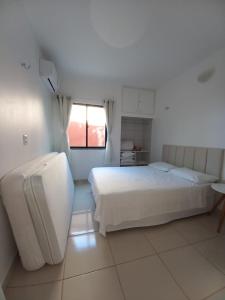 a white bedroom with a bed and a window at Apartamento Porto das Dunas in Aquiraz