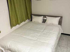 ein Bett mit weißer Bettwäsche und einem grünen Vorhang in der Unterkunft The Guest House Noah in Naha