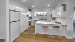 una cocina blanca con electrodomésticos blancos y 2 taburetes en Coastal Escape, en Sussex Inlet