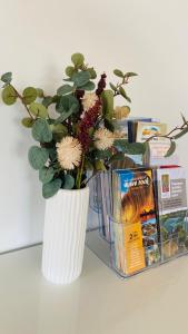 a white vase with flowers in it next to books at The Bungalow - Wave Rock Short Stay in Hyden