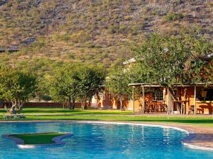 a swimming pool in a park with a mountain in the background at Gondwana Damara Mopane Lodge in Mopane Pos