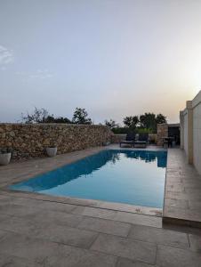 a swimming pool in a yard with a stone wall at Sea Holly Gozo in Nadur