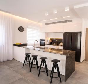 a kitchen with three bar stools and a black refrigerator at Hapalmah One, Jerusalem, Dira 4 in Jerusalem