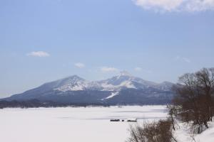 a snow covered lake with a mountain in the background at Urabandai Cranes in Kitashiobara