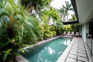 a swimming pool with palm trees and a house at Chez Brolga in Port Douglas