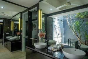 a bathroom with three sinks and two mirrors at Suluban Cliff Bali Villa in Uluwatu