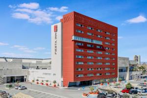 een rood-wit hotelgebouw met een parkeerplaats bij Fiesta Inn Torreon Galerias in Torreón
