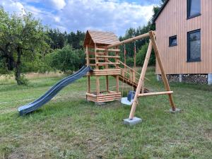 einem Holzspielplatz mit Rutsche und einem Haus in der Unterkunft Baciki 61- domek przy lesie in Baciki Dalsze