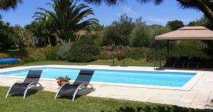 a swimming pool with two chairs and an umbrella at Quinta Pedagogica da Samoqueirinha - Duna Parque Group in Vila Nova de Milfontes