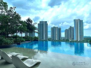 Una gran piscina con sillas blancas frente a una ciudad. en The Elysia Suites, en Nusajaya